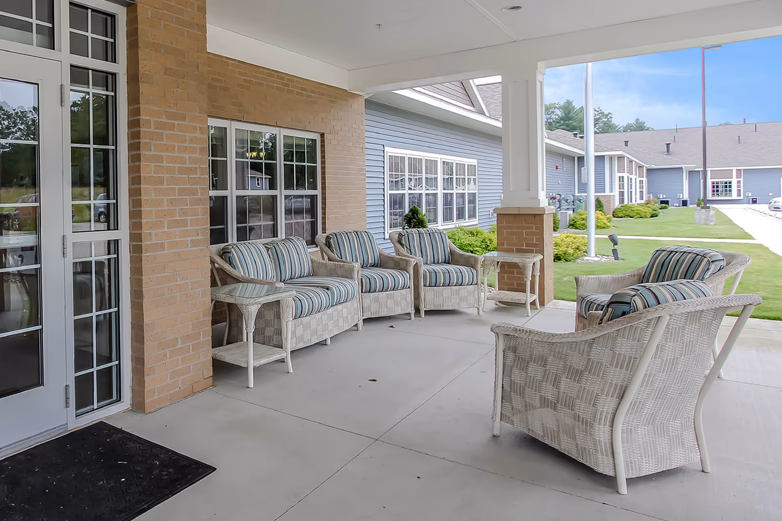 Covered outdoor seating area with white wicker chairs and striped cushions on the front porch of an assisted living building.