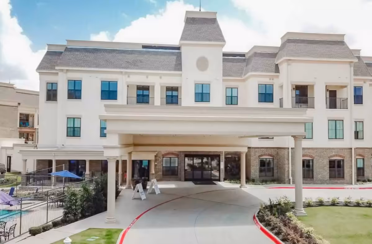 Front exterior of a multi-story senior living building with a covered entrance/porte-cochere and an adjacent outdoor pool area.