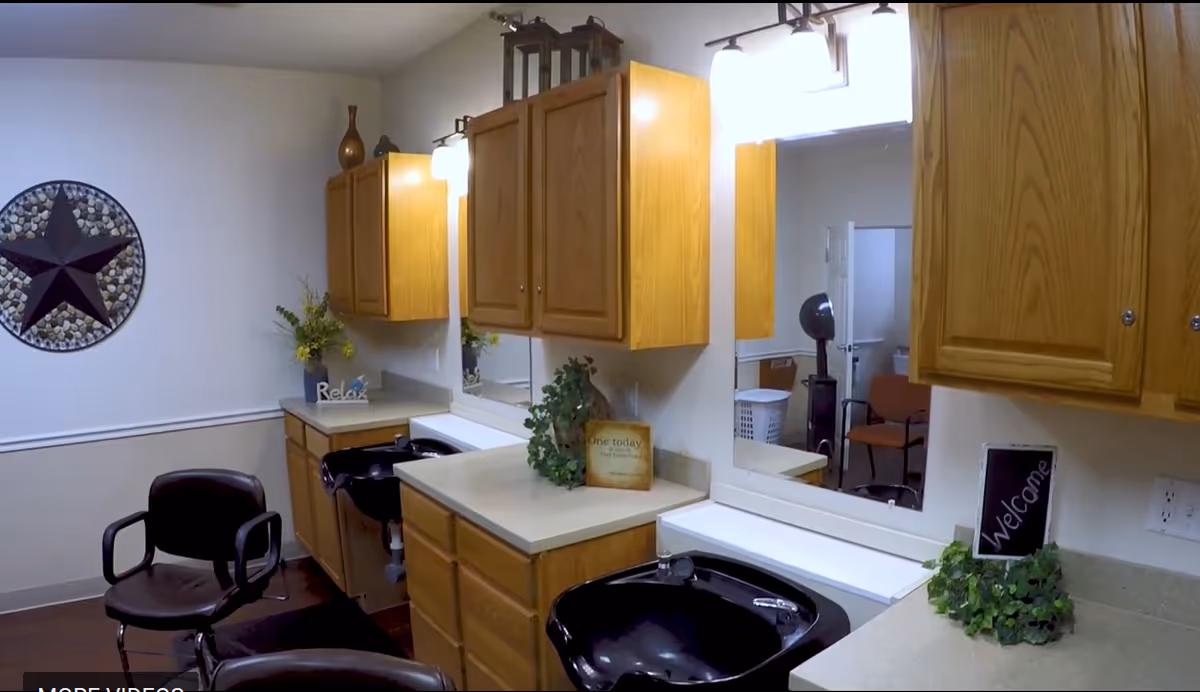Small salon-style hair-washing and styling area with wooden cabinets, mirrors, black shampoo sinks, chairs and decorative plants.