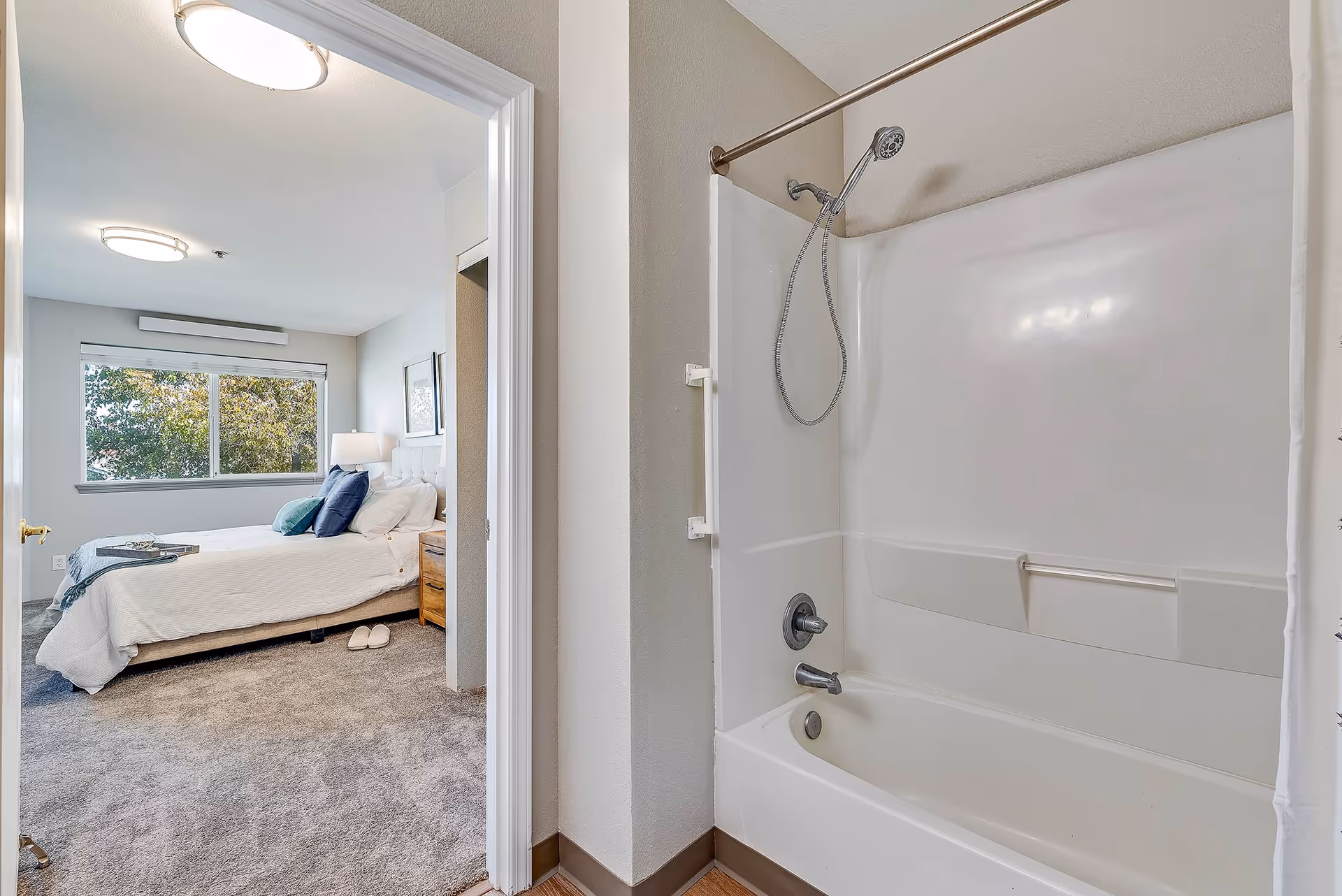 Bathtub and shower in a bathroom with an adjoining bedroom visible through an open door.