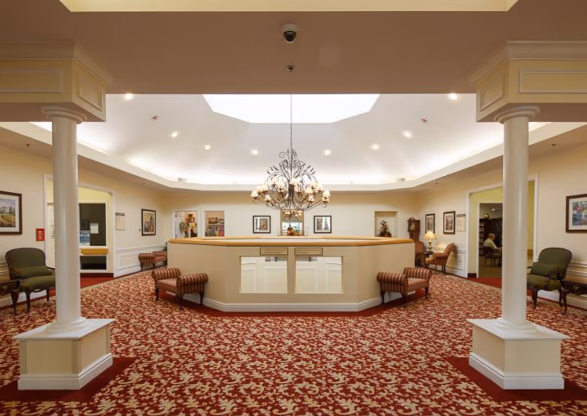 Spacious senior living facility reception lobby with a central desk, chandelier, patterned red carpet and seating.