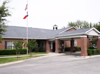 Front exterior of a brick senior living facility with flagpoles and a covered entrance.