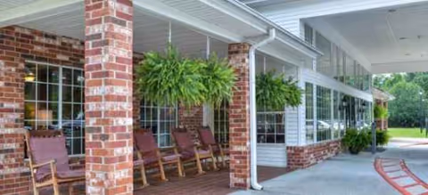 A brick-front exterior with hanging ferns and rocking chairs on a covered porch.