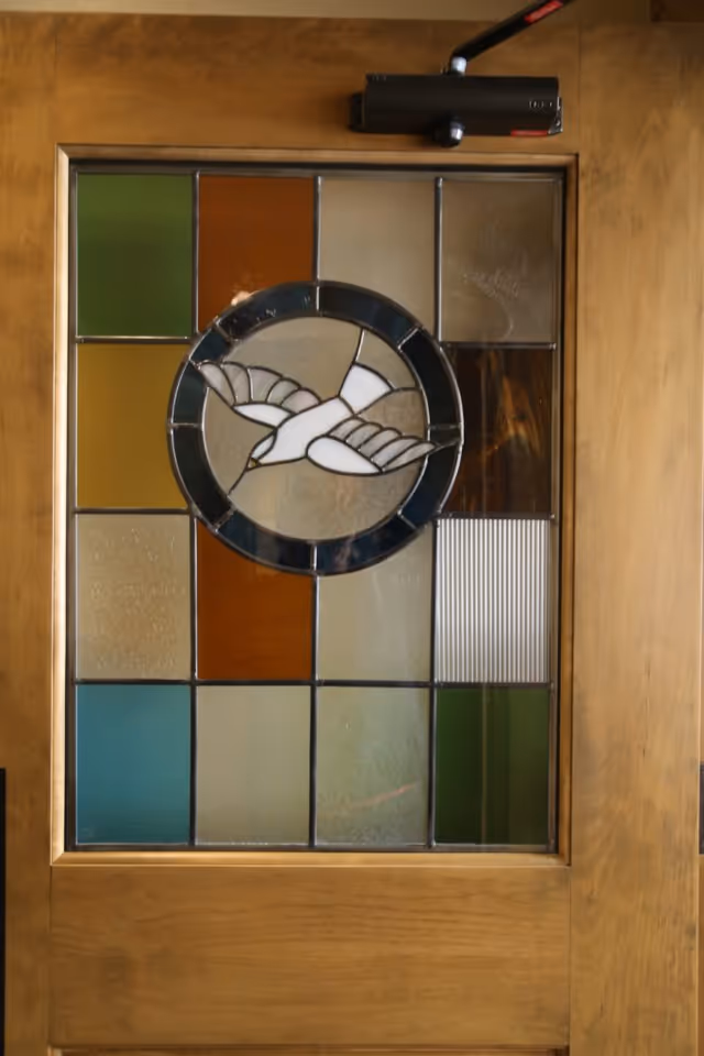 Wooden door with a stained-glass panel featuring a circular white bird motif and multicolored rectangular panes.