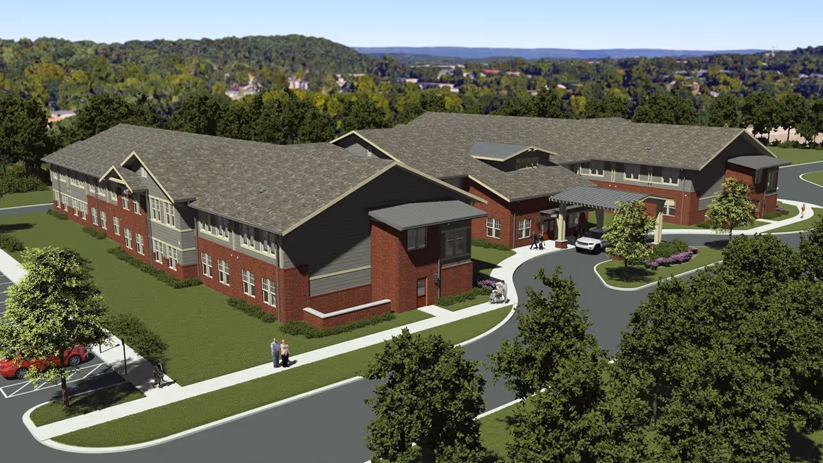 Aerial view of a two-story red-brick senior living building with a circular driveway, landscaping, and surrounding trees.