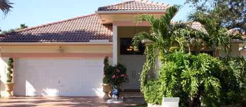 Front exterior of a single-story senior living facility with palm trees and a two car garage.
