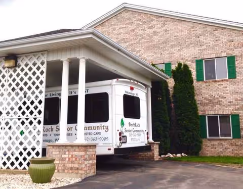 Exterior of Castle Senior Living Birchrock Castle with a covered entrance and parked bus.
