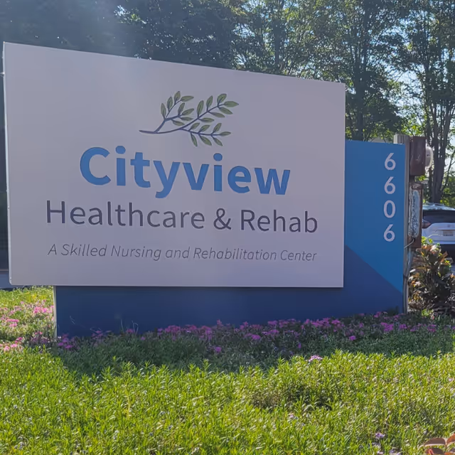 Outdoor sign that reads "Cityview Healthcare & Rehab" set in landscaping with trees and parked cars behind it.