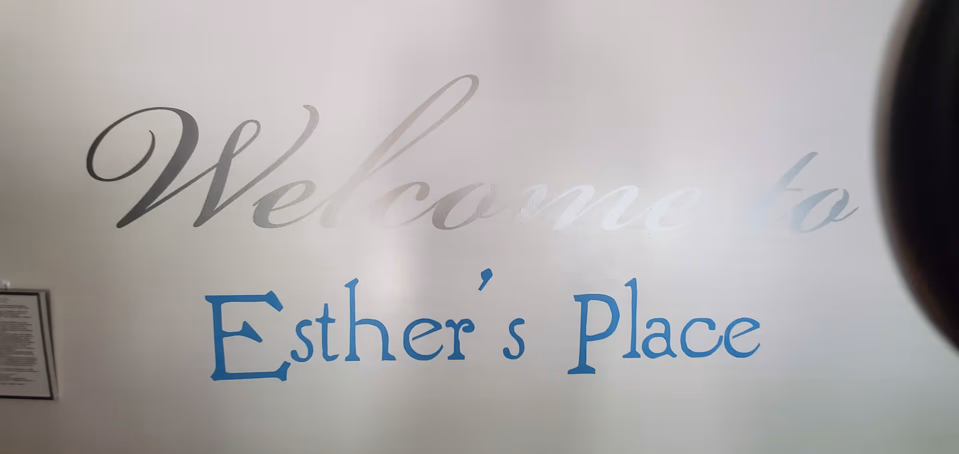 A light-colored wall sign that reads "Welcome to Esther's Place" in decorative fonts.