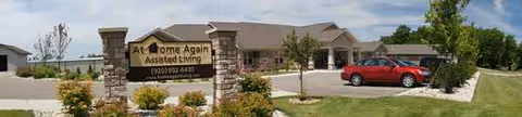 Exterior view of At Home Again Assisted Living building with sign and landscaping.