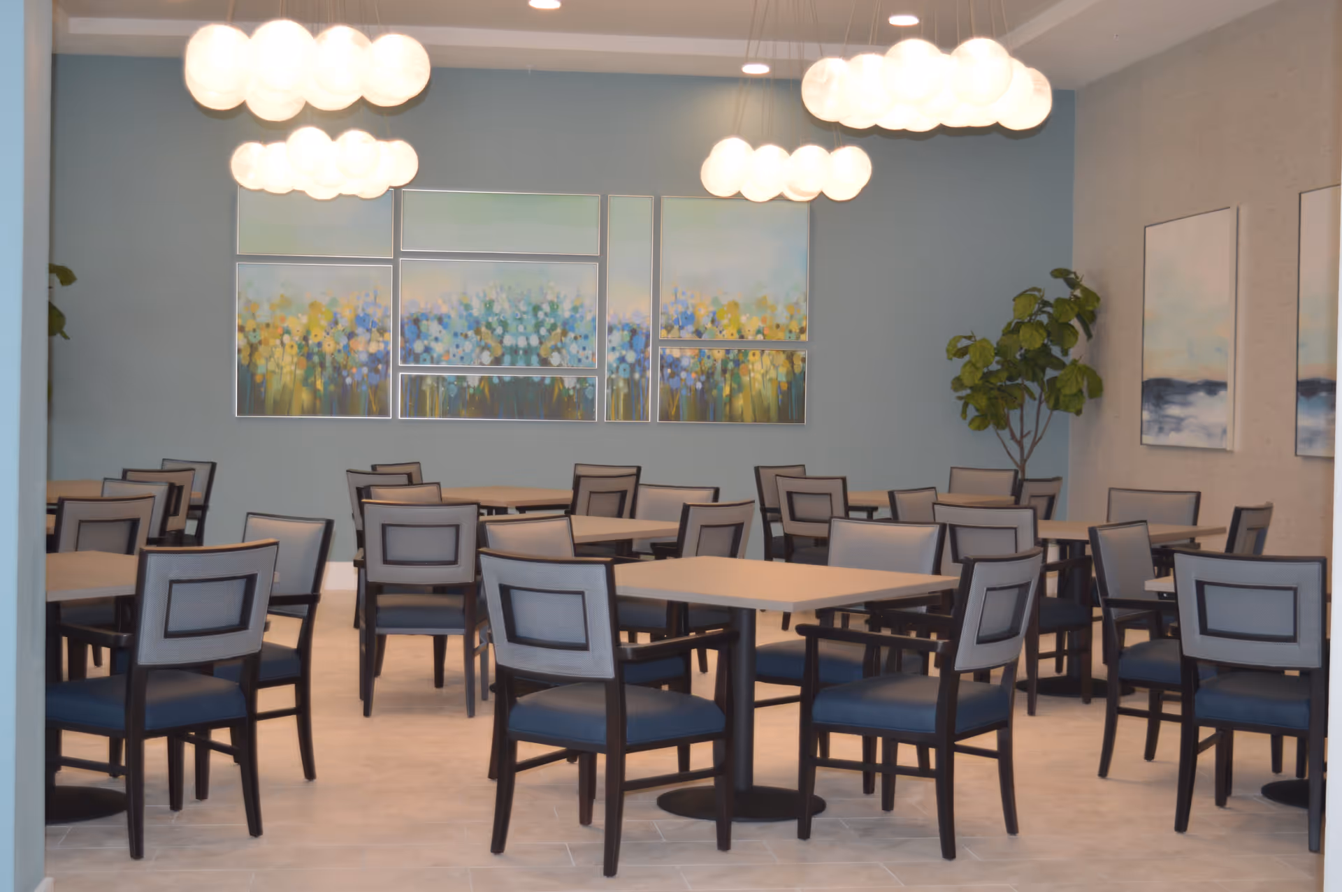 Dining room with multiple tables and chairs, pendant globe lights, colorful wall art, and a potted plant.