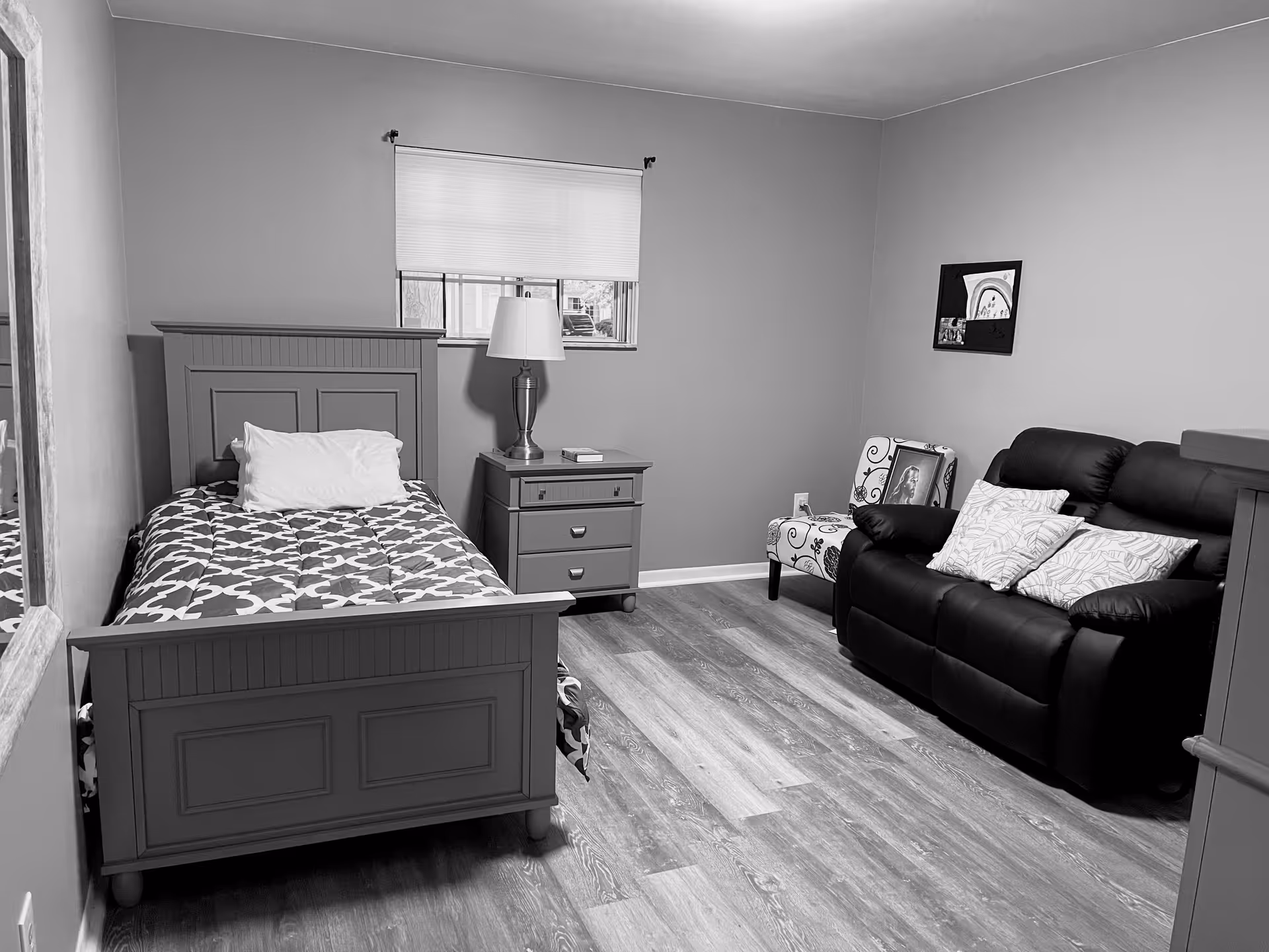 Bedroom in Sara Rose AFC facility featuring a bed, nightstand, lamp, and a leather sofa.
