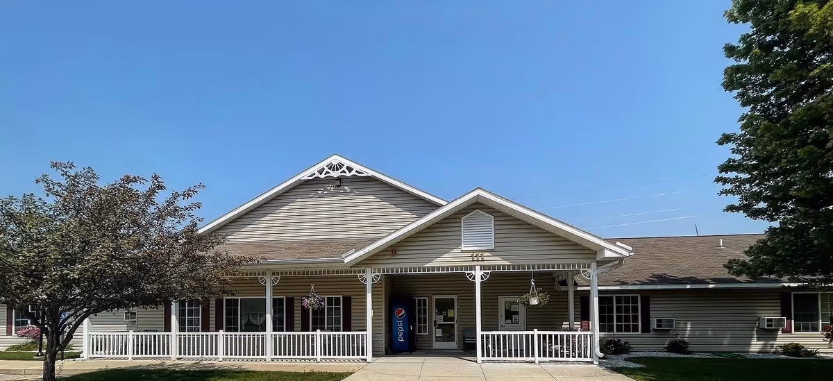 Single-story facility building with a covered front porch, white railing, peaked roof and a Pepsi vending machine at the entrance under a clear blue sky.