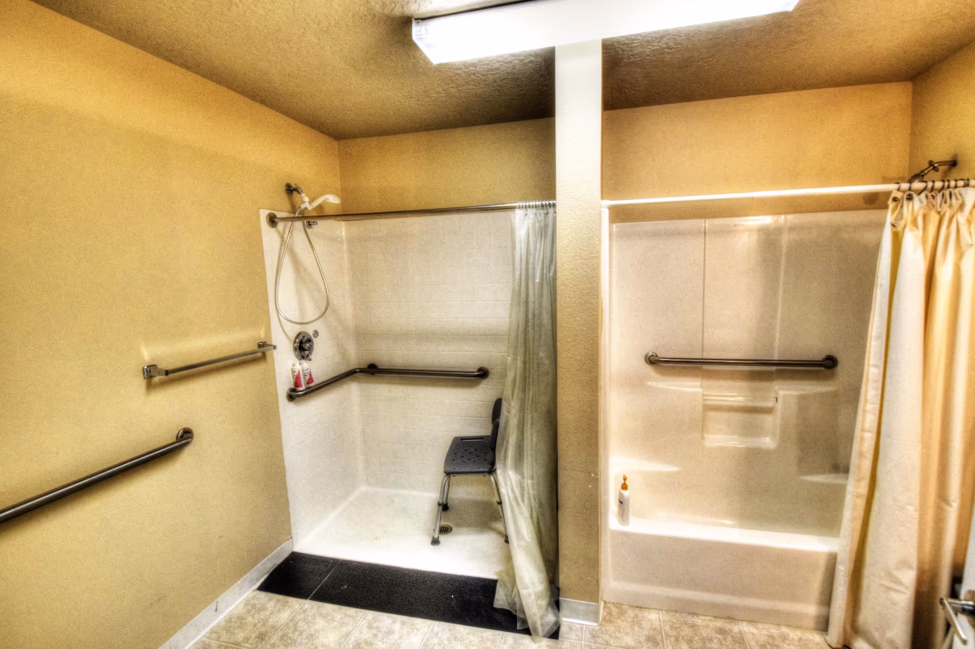 Accessible bathroom with two shower stalls, grab bars, a shower chair, and curtains.