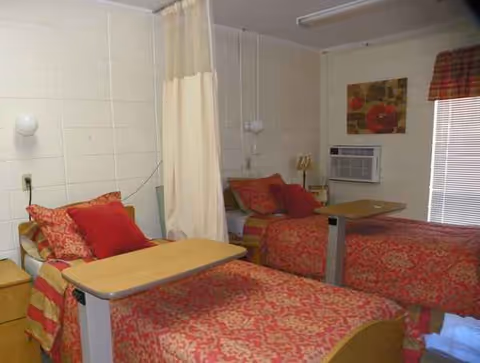 Two twin beds with red patterned bedding, overbed tables, and a curtain divider in a room.