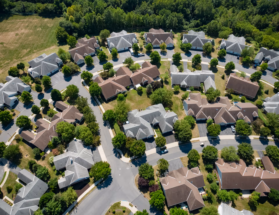 Aerial view of a residential community with multiple houses arranged along curved streets, surrounded by trees and greenery.