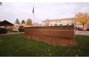 Brick entrance sign for Elm Crest Senior Living Community on a grassy lawn with the facility building, flagpole, and gazebo in the background.