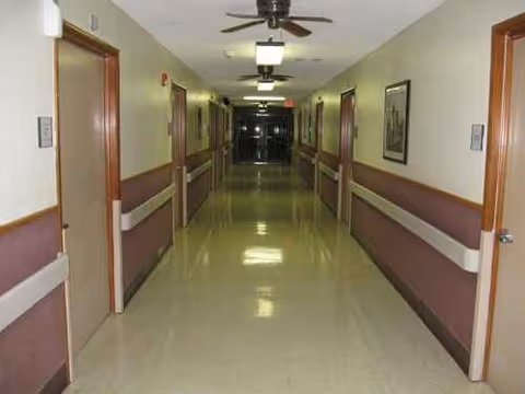 Long hallway in a senior living facility with doors along both sides and ceiling lights.