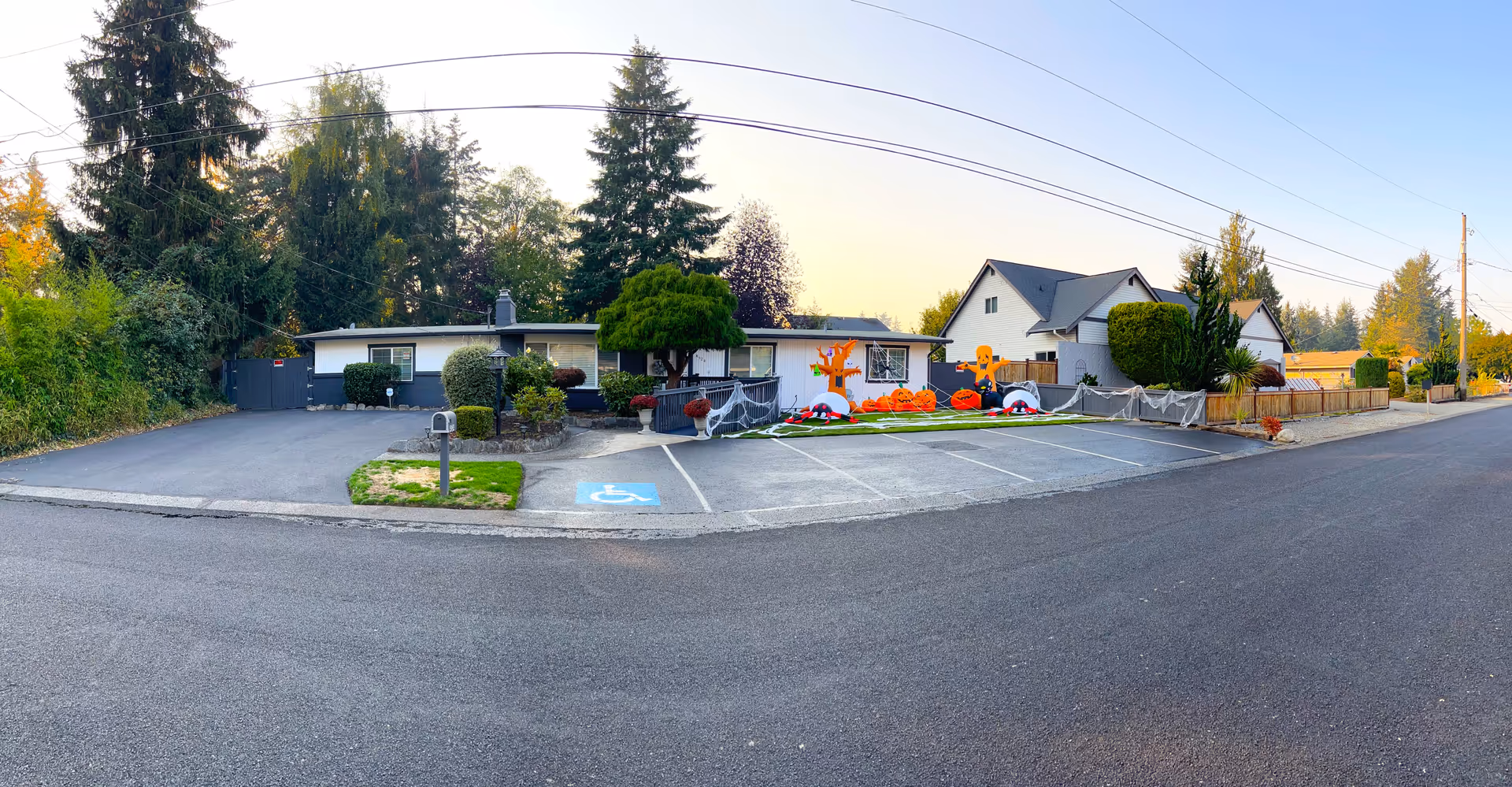 Front exterior of a single-story senior care home with a paved parking area, accessible parking spot, and Halloween decorations on the lawn.