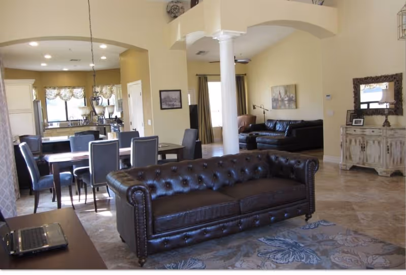 Open-plan living area with a tufted leather sofa, dining table, kitchen in the background and decorative furnishings.