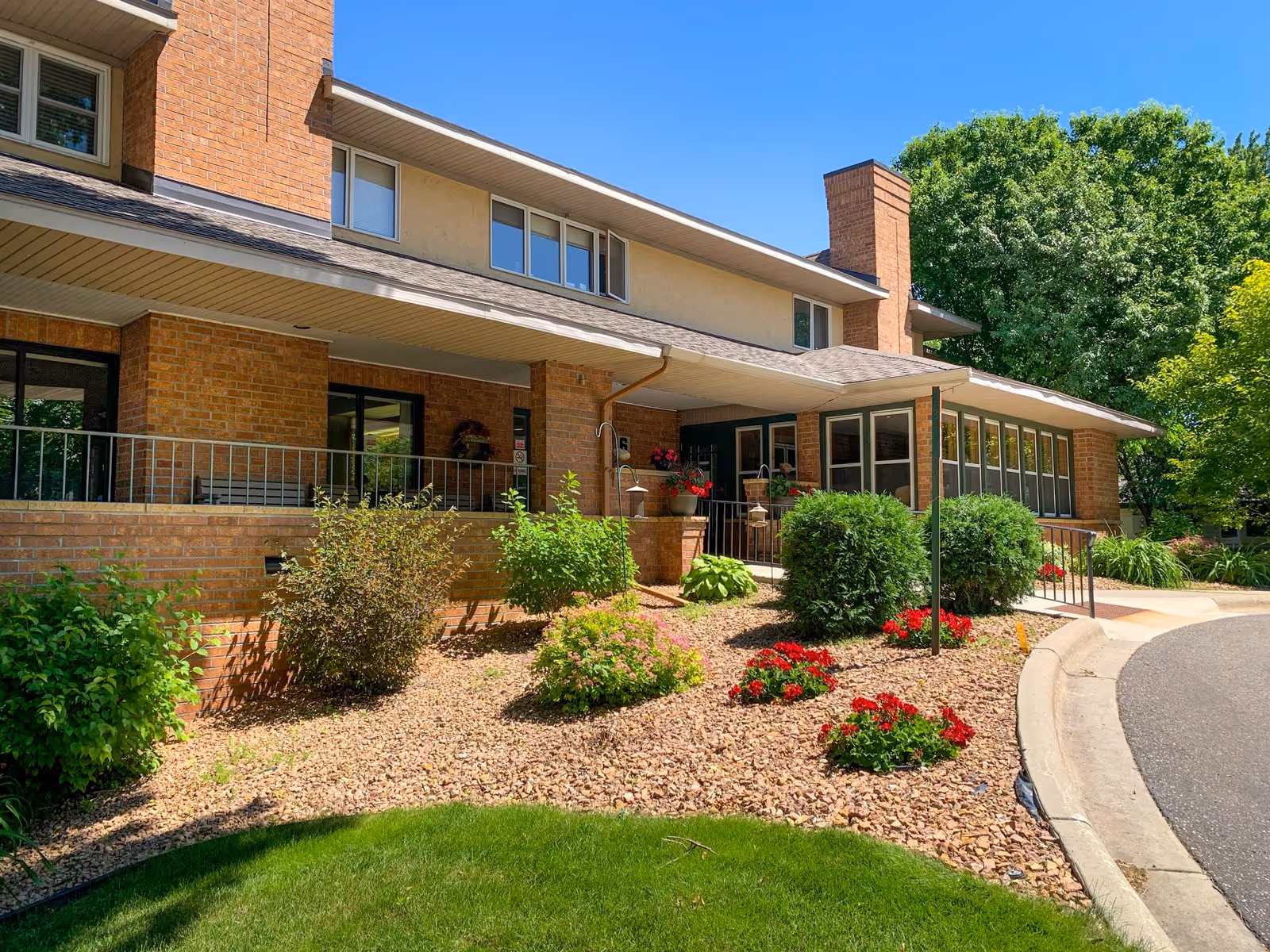Brick-front entrance of Parkview Court with a covered porch, landscaped flower beds, and a curved driveway.