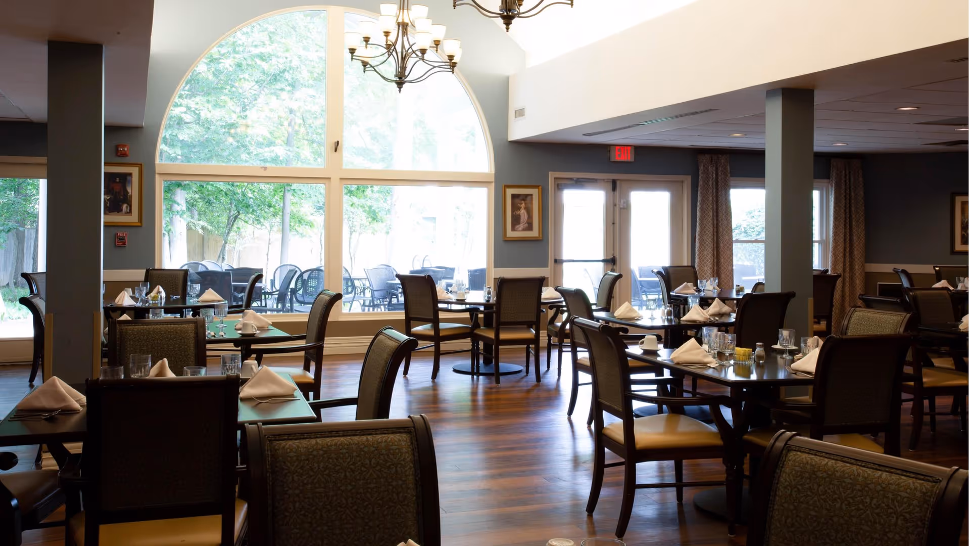 Bright dining room with multiple set tables and chairs, a large arched window, and a chandelier.