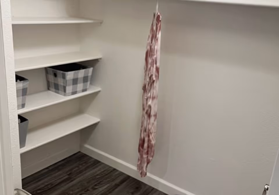 Small walk-in closet with white built-in shelves holding storage baskets and a single hanging scarf.