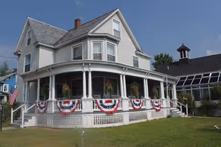 Front exterior of The Villager Assisted Living with a wraparound porch and bunting.