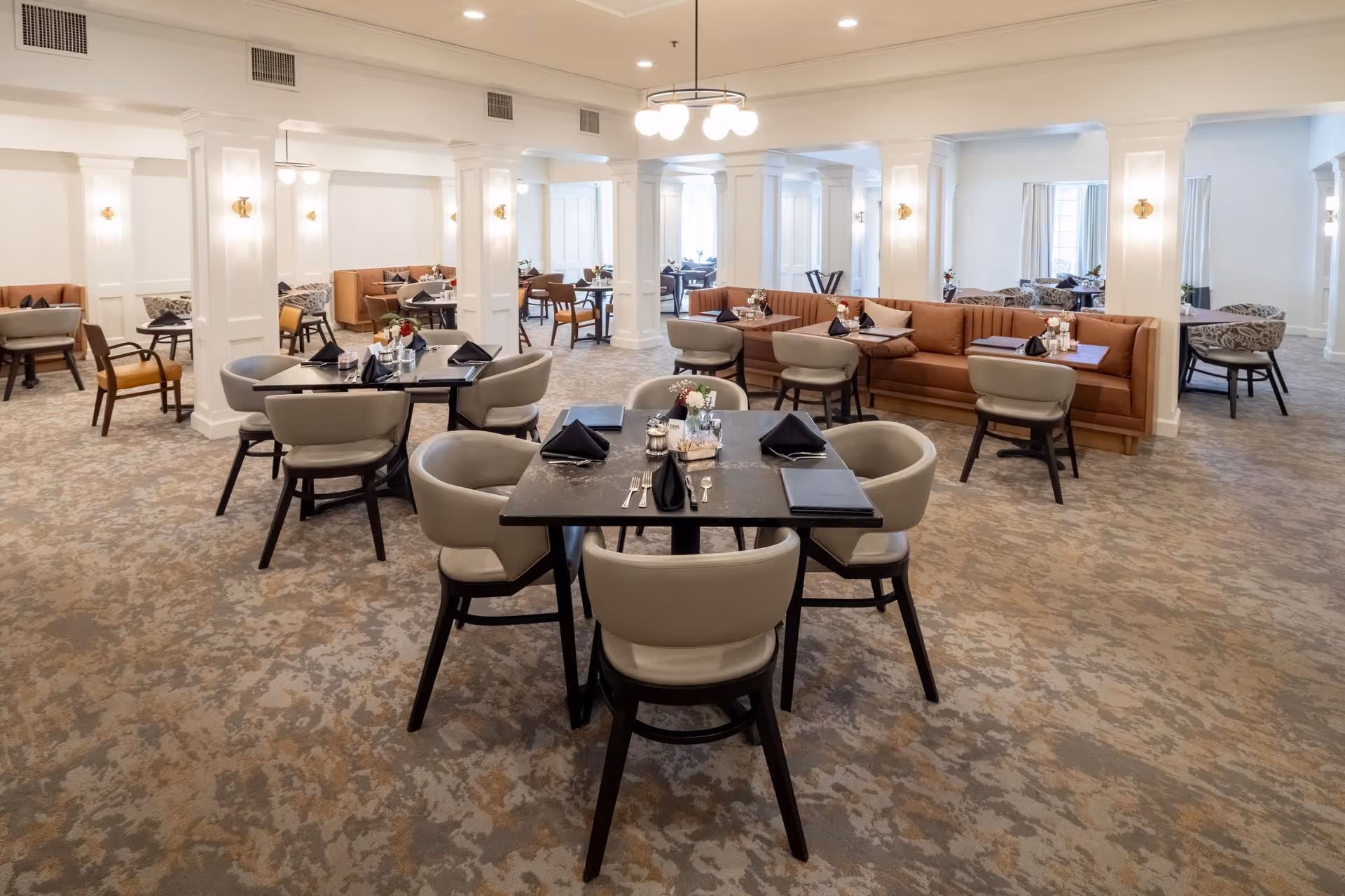 Bright, spacious dining room with modern tables, upholstered chairs, banquette seating, and ambient lighting.