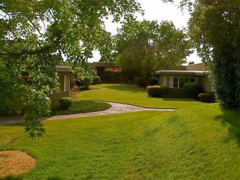 Well-manicured lawn with curved walkway and low-rise retirement buildings framed by trees.