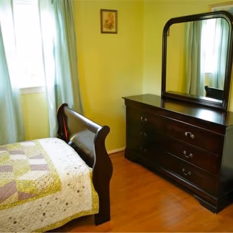 Small bedroom with a wooden sleigh bed covered by a quilt and a dark wood dresser with a mirror.