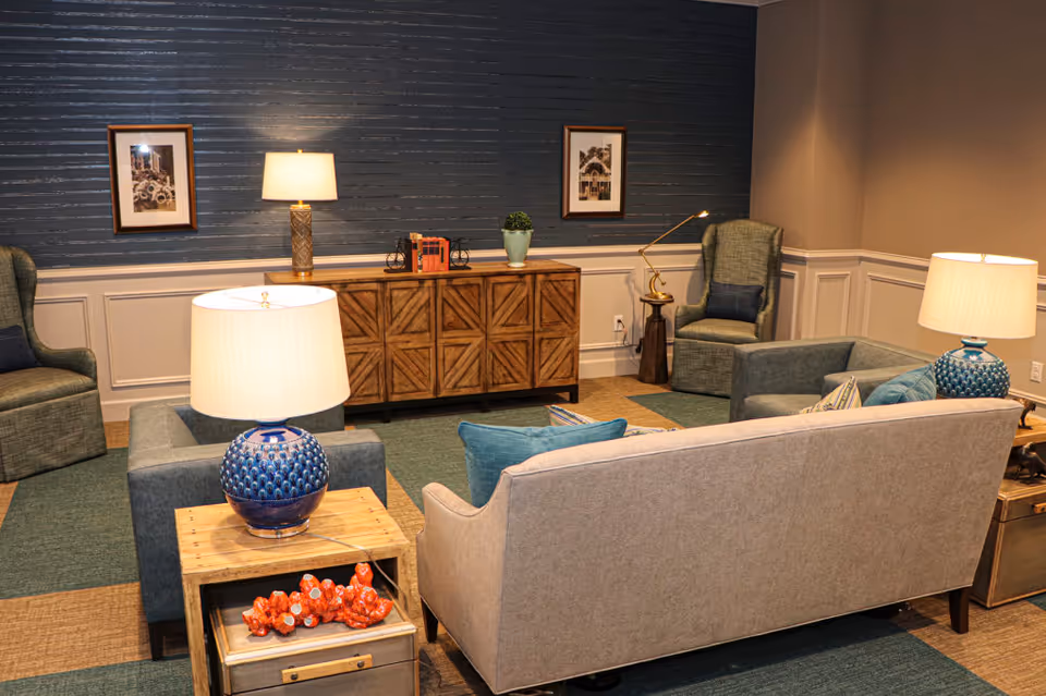 Well-appointed lounge with sofas, armchairs, side tables, lamps, and a wooden console against a blue accent wall.