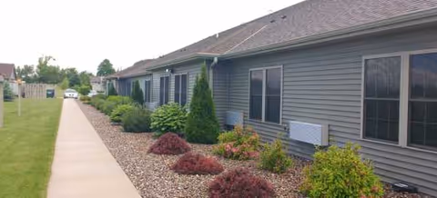 Exterior view of Field of Dreams Assisted Living with walkway, gravel beds, and shrubs.