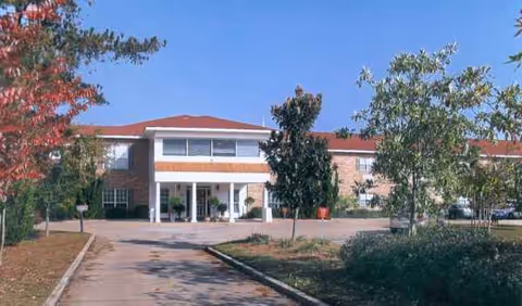 Front view of Brandon Court Nursing facility, brick building with entrance columns, trees, and driveway.