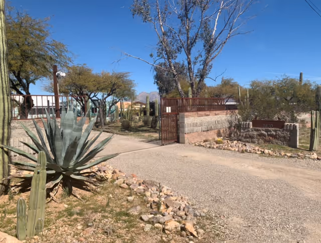 Entrance driveway to a facility with desert landscaping including cacti and trees, a gated fence, and a sign with the number 7510 under a clear blue sky.
