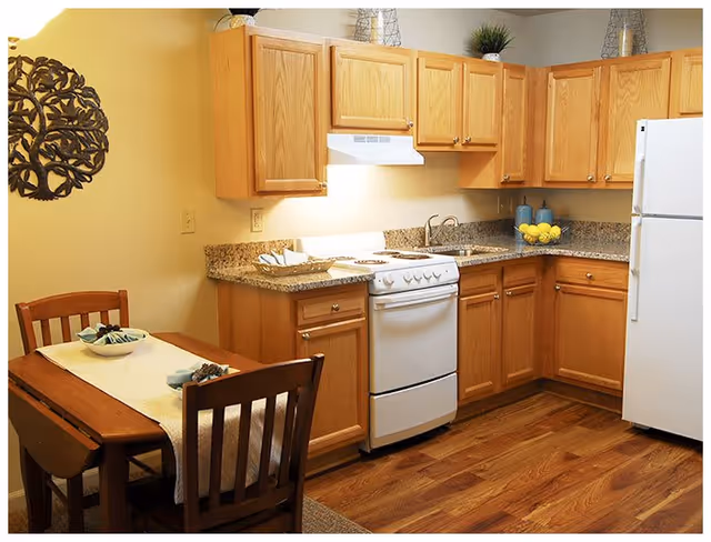 A cozy kitchen featuring wooden cabinets, a white stove, and a dining table with two chairs. The countertop is adorned with dishes and a bowl of lemons, creating a warm and inviting atmosphere.