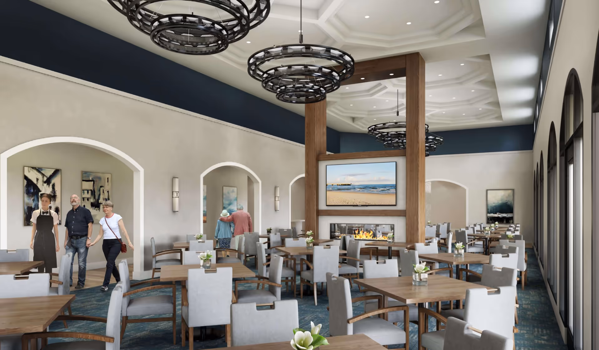 Spacious dining room with rows of tables and chairs, decorative chandeliers, a central fireplace and a few people walking.