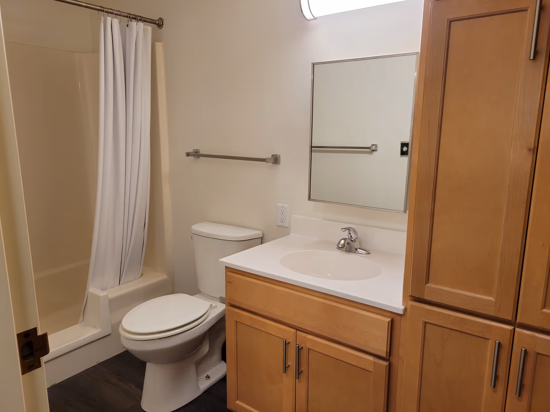 Small bathroom with a toilet, sink and vanity, mirror, shower with a white curtain, and wooden cabinets.