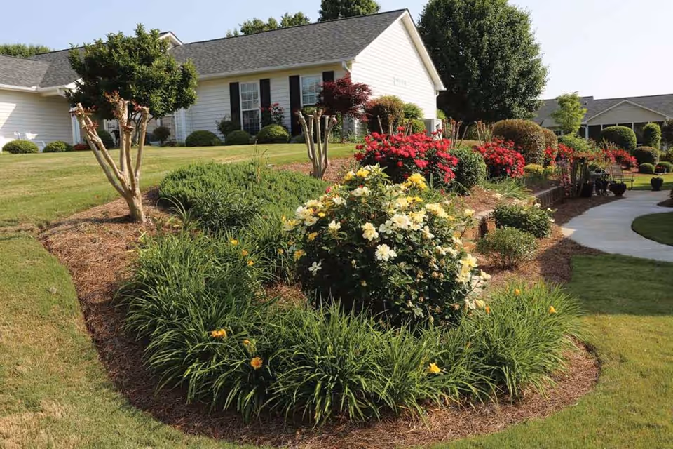 Landscaped front yard with colorful flower beds, a curved walkway, and a white single-story building in the background.