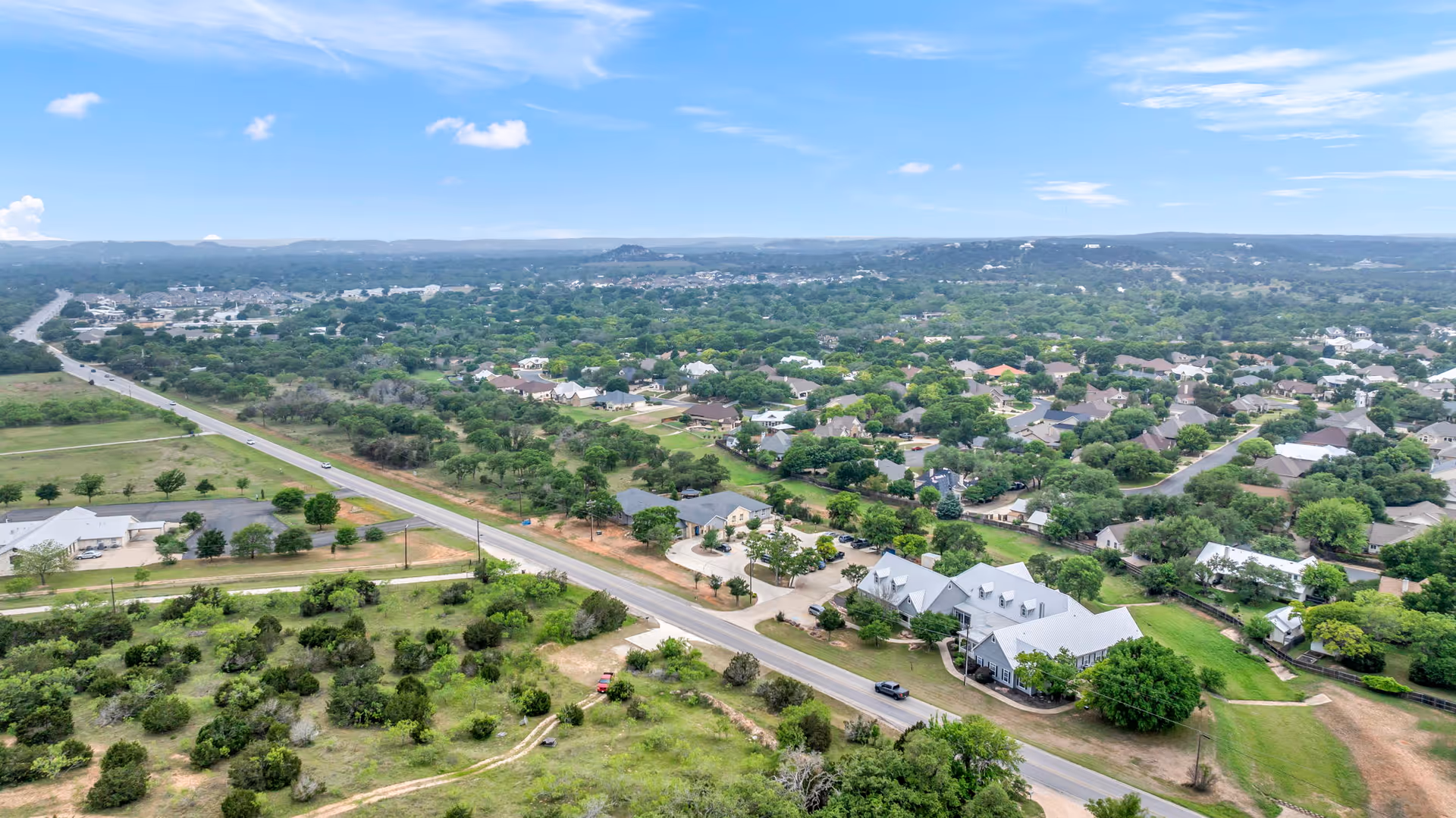 Aerial view of a suburban neighborhood and surrounding greenery with a main road running through it.