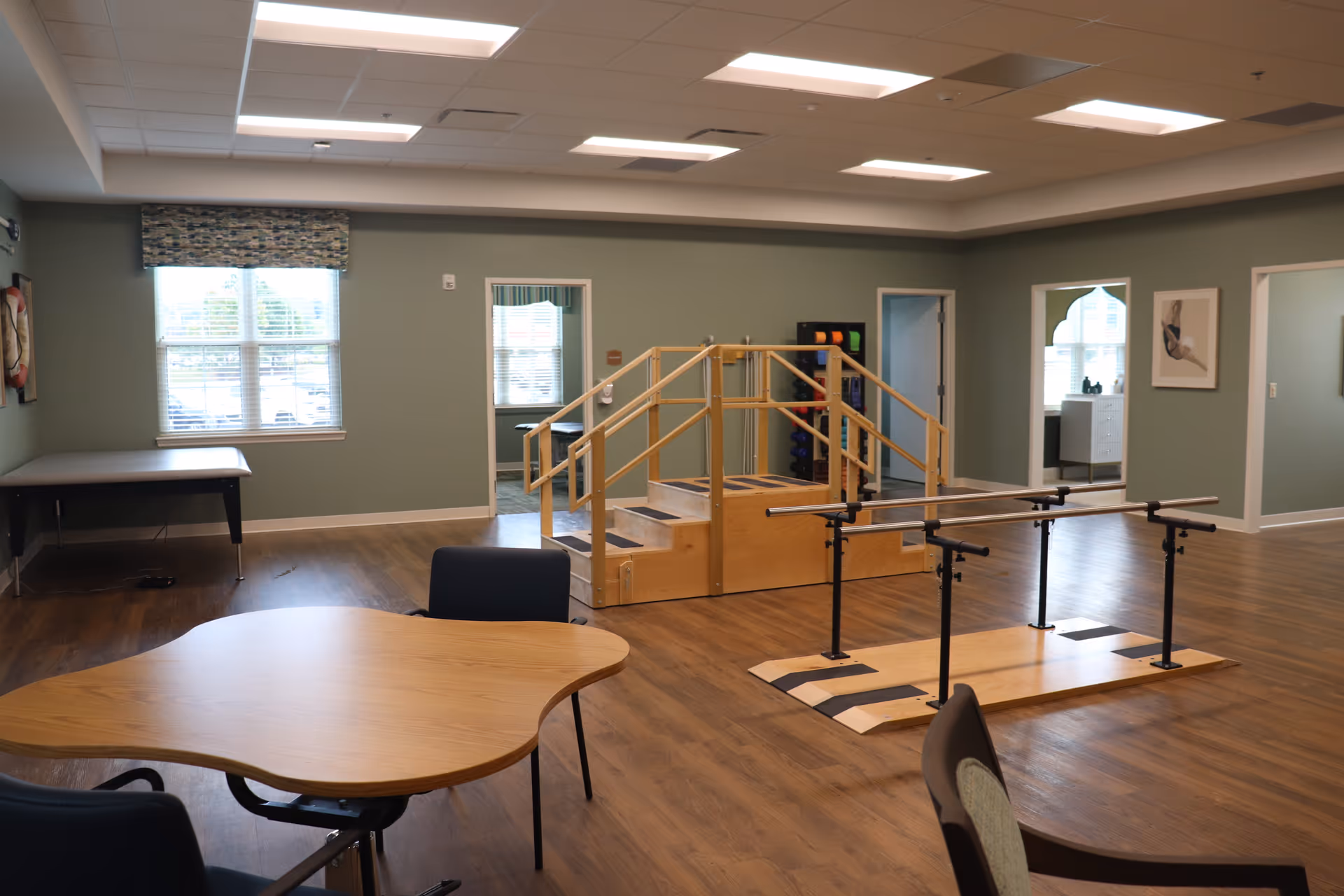 Spacious interior therapy room with parallel bars, practice stairs, tables and chairs in a senior living facility.