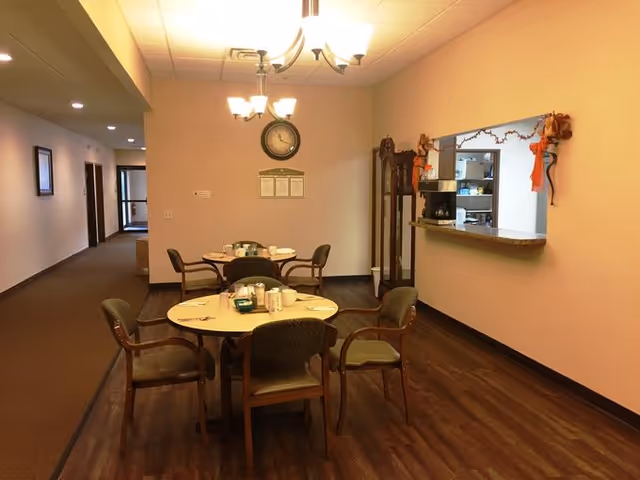 Small dining area with two round tables set for meals, chairs, a service window, and a wall clock.