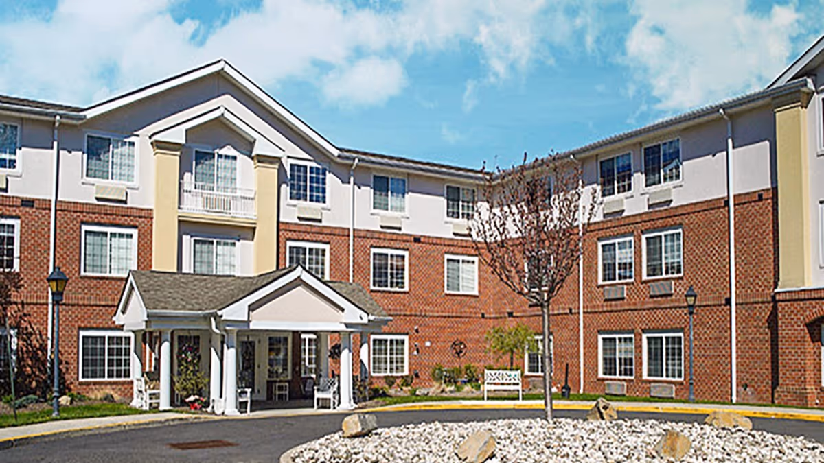 Three-story brick senior living building with a covered entrance and a circular driveway with landscaping.
