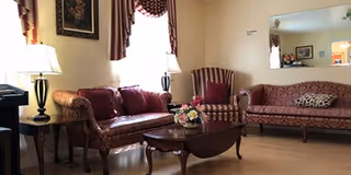 A cozy living room with a patterned sofa, a striped armchair, a wooden coffee table with a floral centerpiece, a side table with a lamp, and a large mirror on the wall reflecting part of the room.