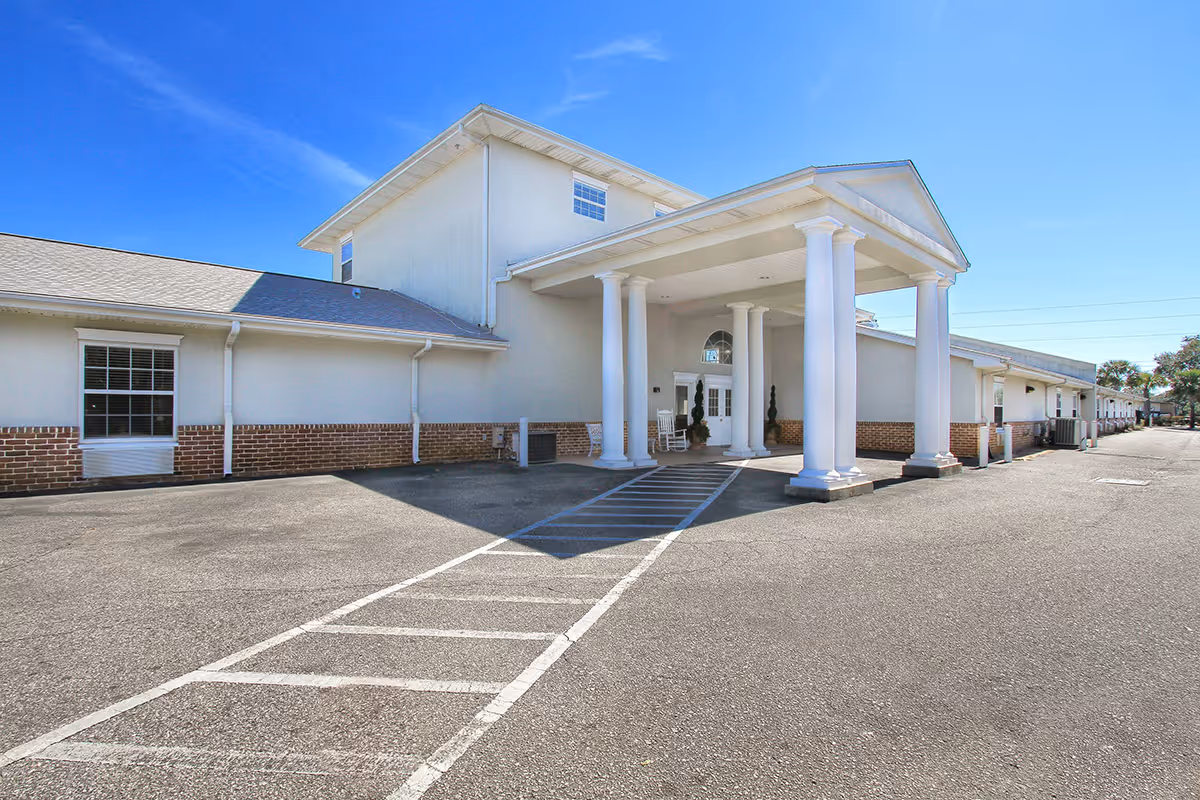 Front entrance of an assisted living facility with white columns, a covered porte-cochere, and a paved parking area.