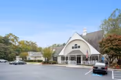 Front exterior view of Governors Glen facility showing a large building with a peaked roof, an entrance with glass doors, an American flag, several parked cars, and trees surrounding the parking area under a clear blue sky.