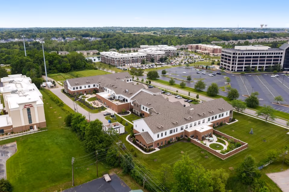 Aerial view of a senior living facility named Montage Mason surrounded by green lawns, trees, parking lots, and nearby buildings under a clear sky.
