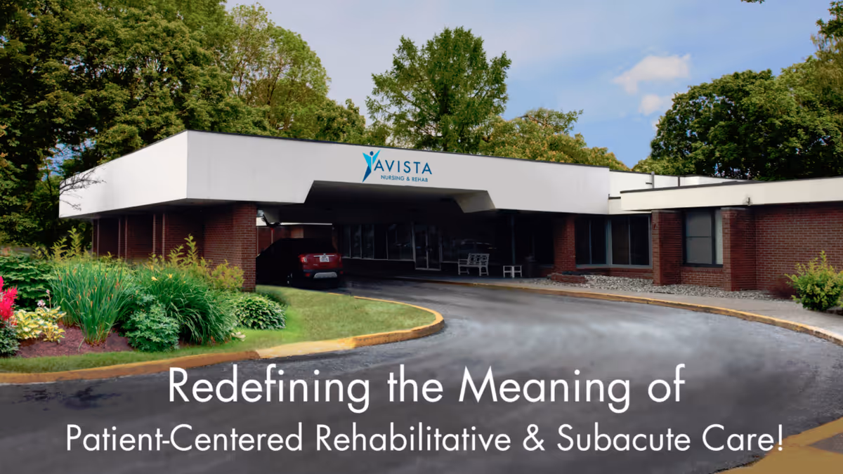 Exterior view of Avista Nursing and Rehab facility showing a single-story building with a covered entrance, surrounded by greenery and trees under a partly cloudy sky.