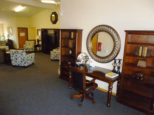 An interior lounge with a desk, chairs, tall bookshelves, and a circular mirror.