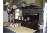 Commercial kitchen showing a large industrial stove with pots and hanging pans above a prep counter.
